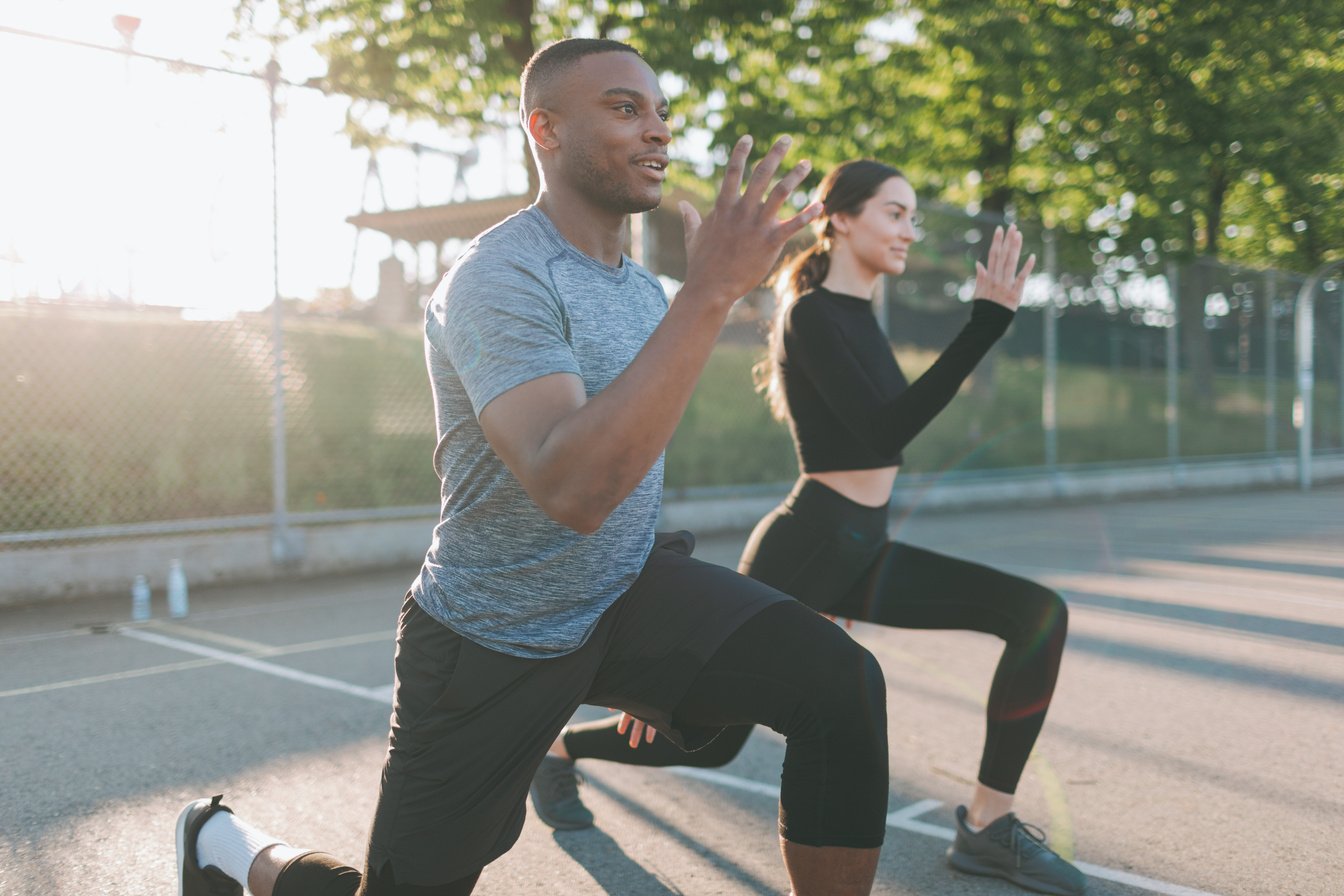 Man and woman in fitness attire performing outdoor squats during a sunset workout session, focusing on health and fitness goals